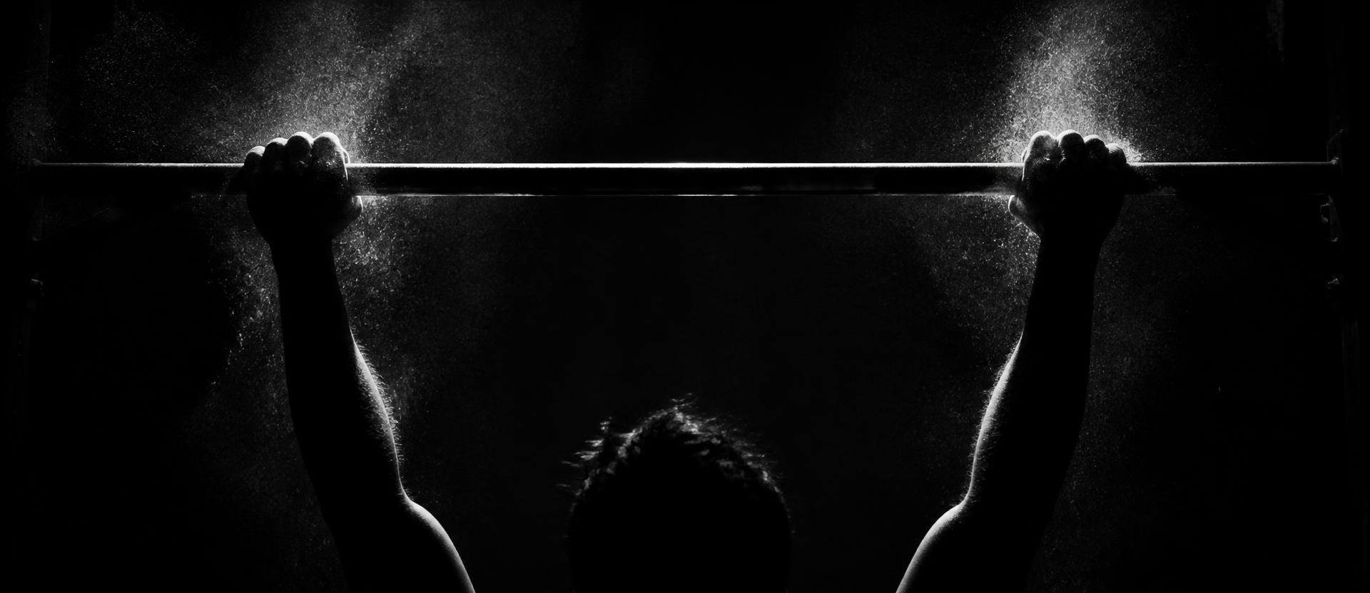 Chalked hands gripping a steel pull-up bar in low light